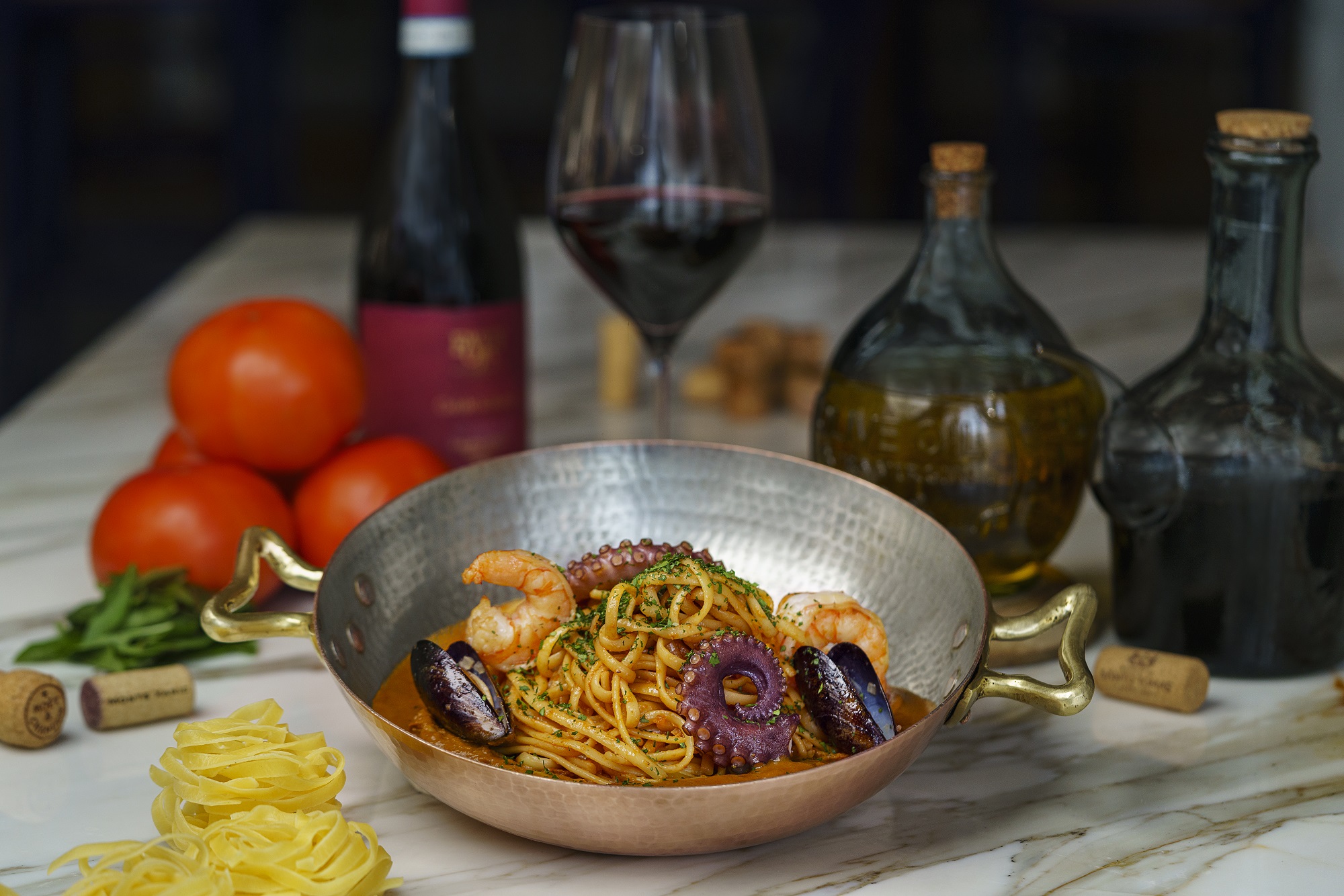 Seafood pasta in copper pan; wine and ingredients seen at; Cello cucina italiana restaurant.